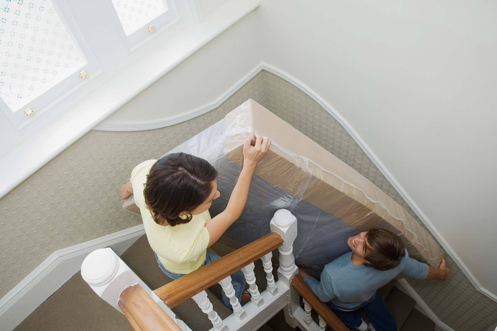 MRArticleMovingYourMattress MattressReviewscom Image of two people moving their mattress up stairs in a house